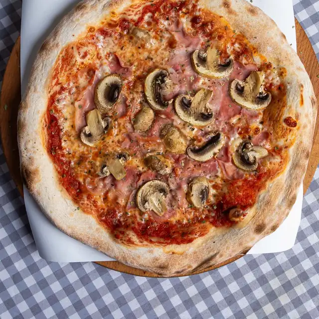 Pizza capricciosa z szynką i pieczarkami na drewnianej desce
