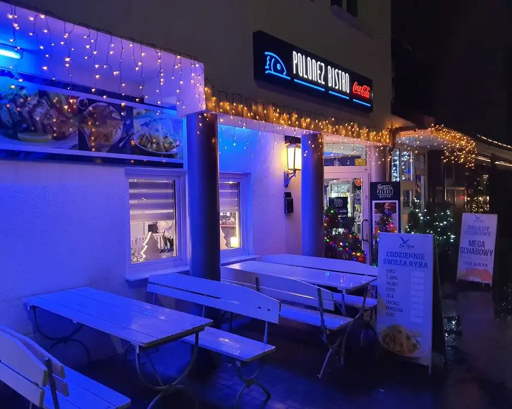 Wejście do Bistro Polonez nocą, podświetlone na niebiesko, z ławkami przed lokalem